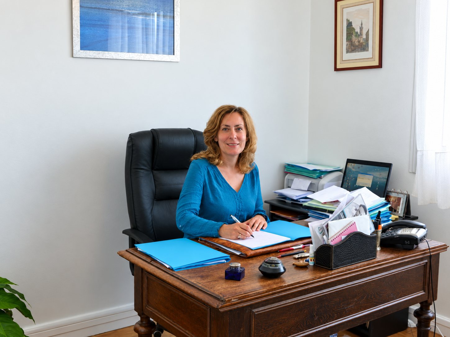 Me Sophie Lemonnier à son bureau, souriante, vêtue d’un haut bleu, un stylo à la main devant un dossier ouvert